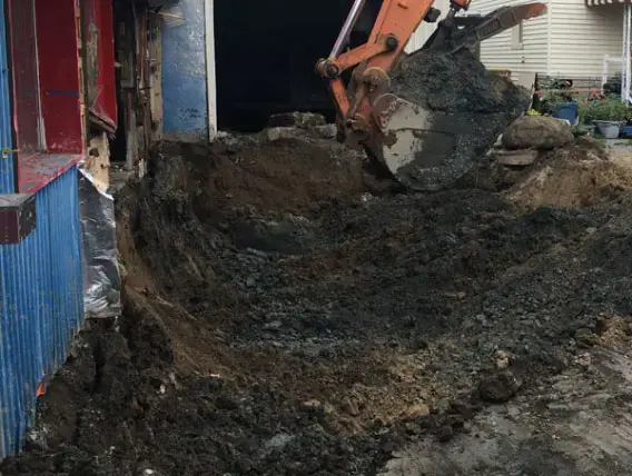 Excavatrice chargeant des sols contaminés près d'un conteneur de chantier, décontamination de station-service